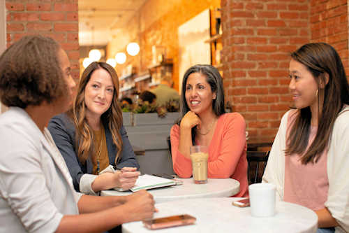 4 women sitting at tables in conversation 4 women sitting at tables in conversation